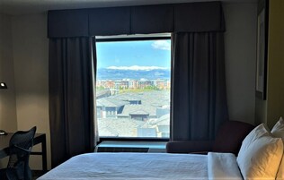Habitación de hotel con una ventana grande, una cama, una silla y un escritorio.