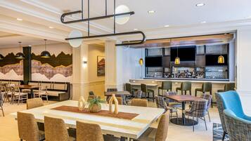 A modern hotel lobby with a bar area, dining tables, and comfortable seating.