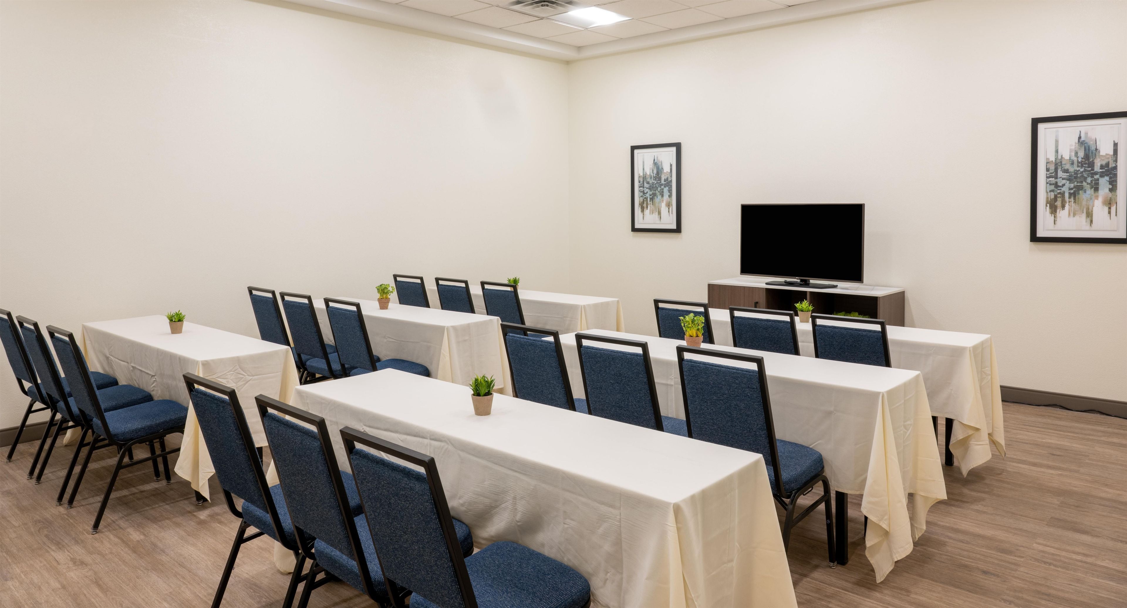 A conference room with multiple tables and chairs, a flat-screen TV, and framed artwork on the walls.