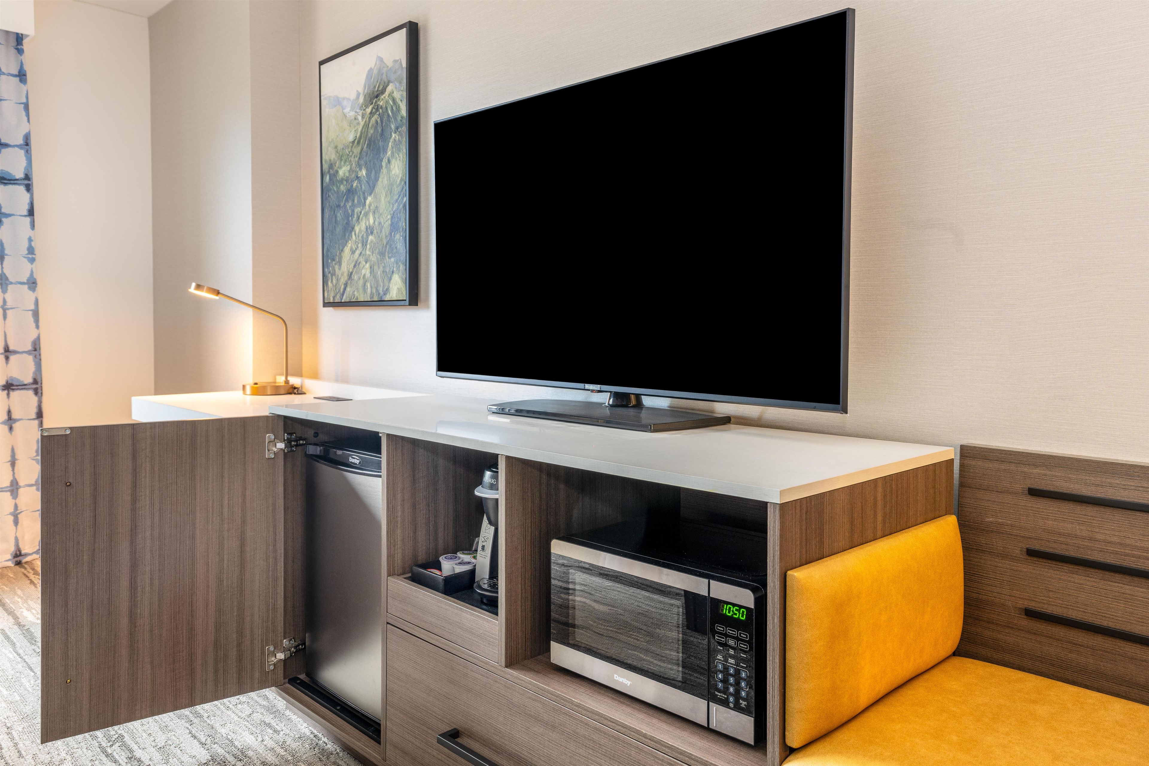 A modern kitchen with a built-in microwave, a flat-screen TV, and a wooden cabinet.