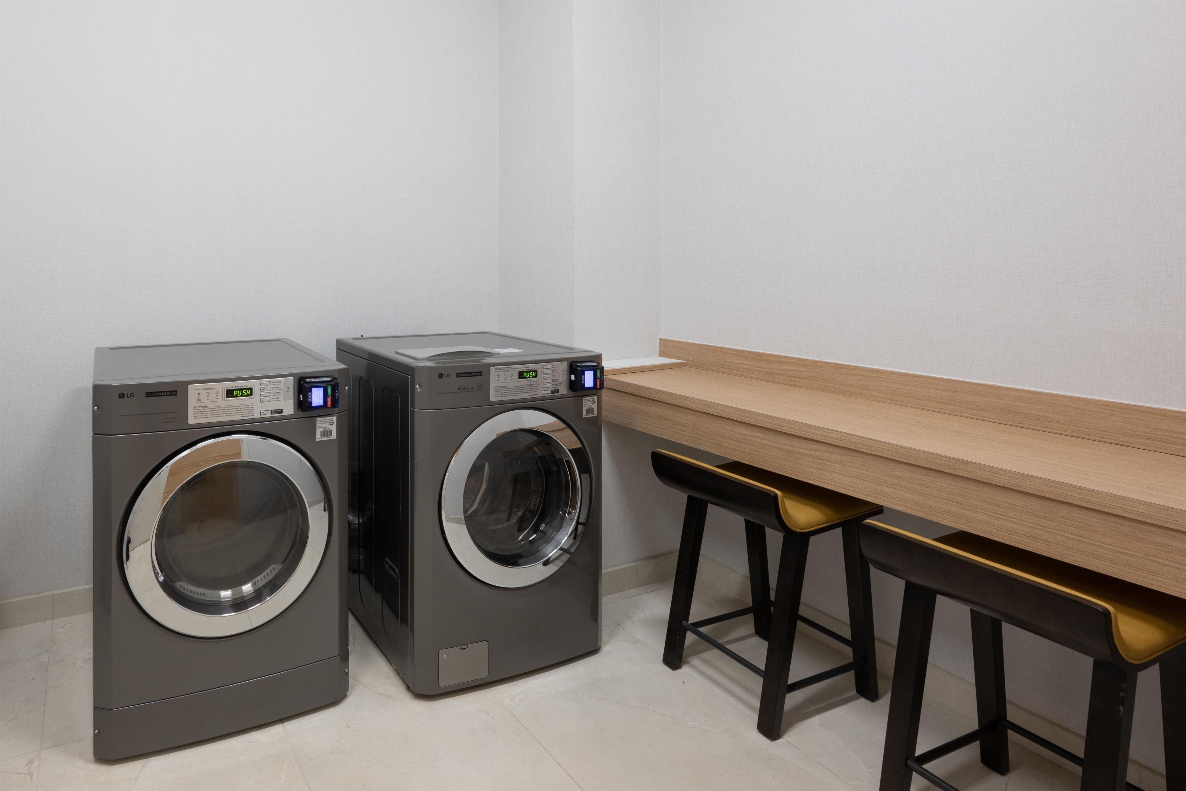 A laundry area with two front-loading washing machines and a wooden table with black barstools.