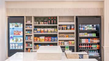 A self-service kiosk with refrigerated sections on either side, stocked with snacks, beverages, and packaged goods.