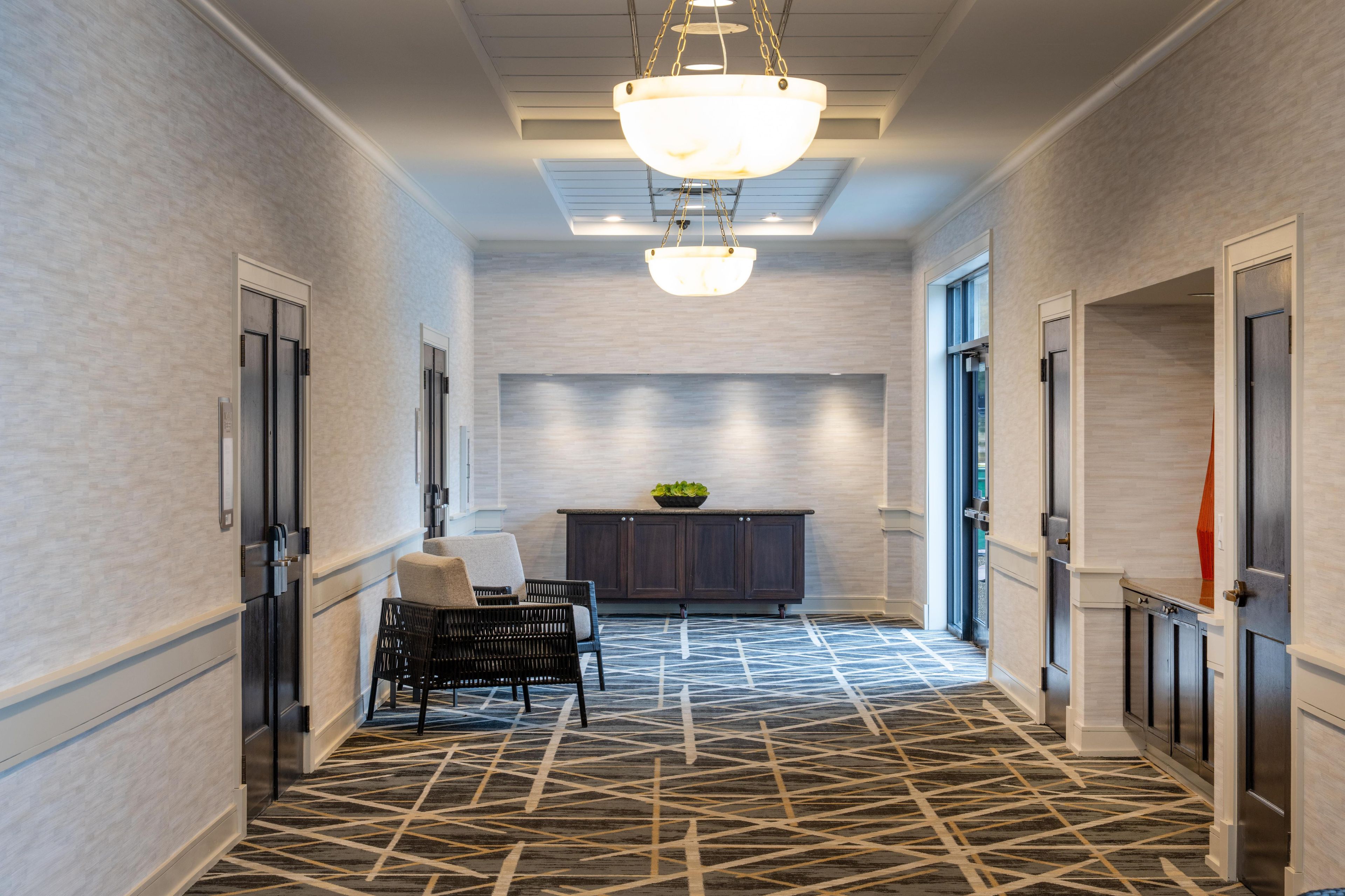 A hallway with a patterned carpet, a bench, a cabinet, and a chandelier.