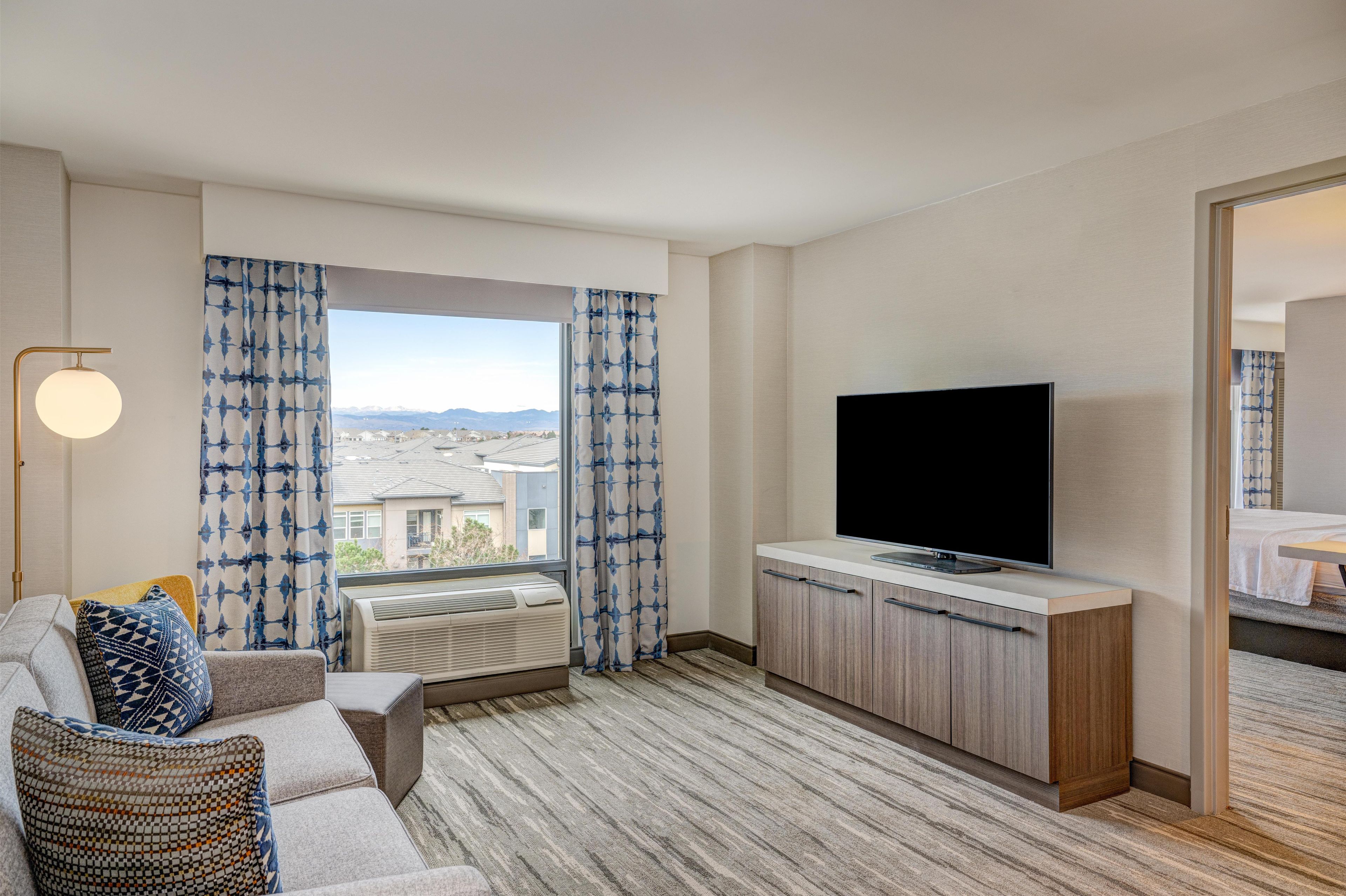 Ein modernes Hotelzimmer mit großem Fenster, Flachbildfernseher, einer Couch und einem Holzkasten.