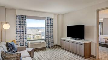 Ein modernes Hotelzimmer mit großem Fenster, Flachbildfernseher, einer Couch und einem Holzkasten.