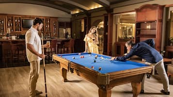 A pool table in a room with wooden flooring and bar area.
