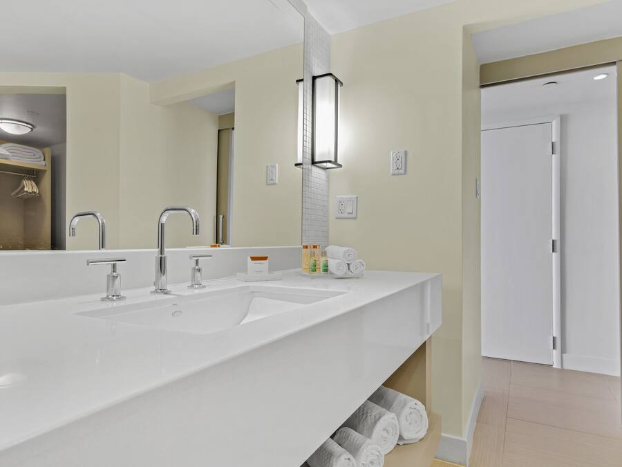 Un baño moderno con un lavamanos grande blanco, dos grifos, un espejo y un perchero para toallas.