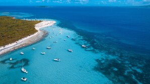 An aerial view of a coastal area with a beach, boats, and clear blue waters.