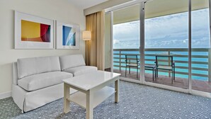 A hotel room with a balcony, a sofa, a table, and two framed artworks.