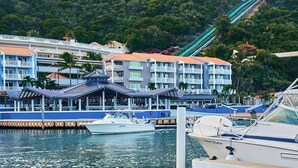 A marina with boats docked, a water slide, and buildings with balconies and outdoor seating.