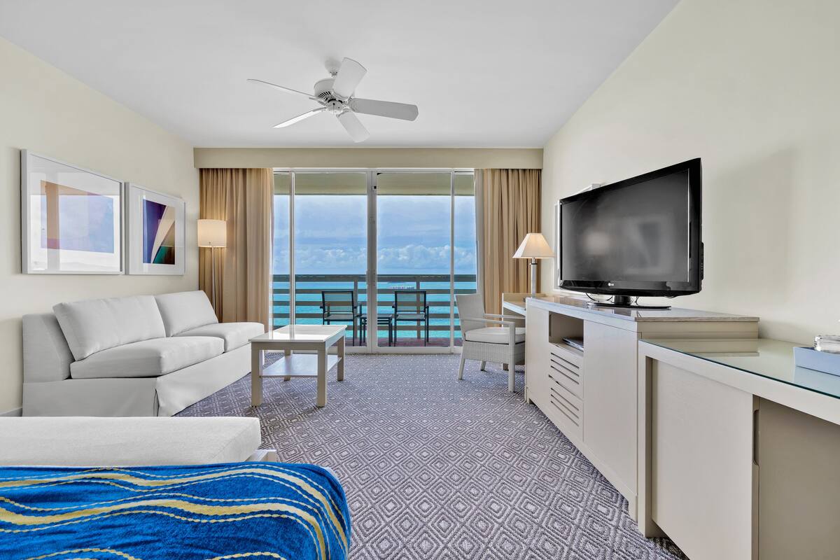 Una habitación de hotel con balcón, cama, televisor, escritorio y sofá.