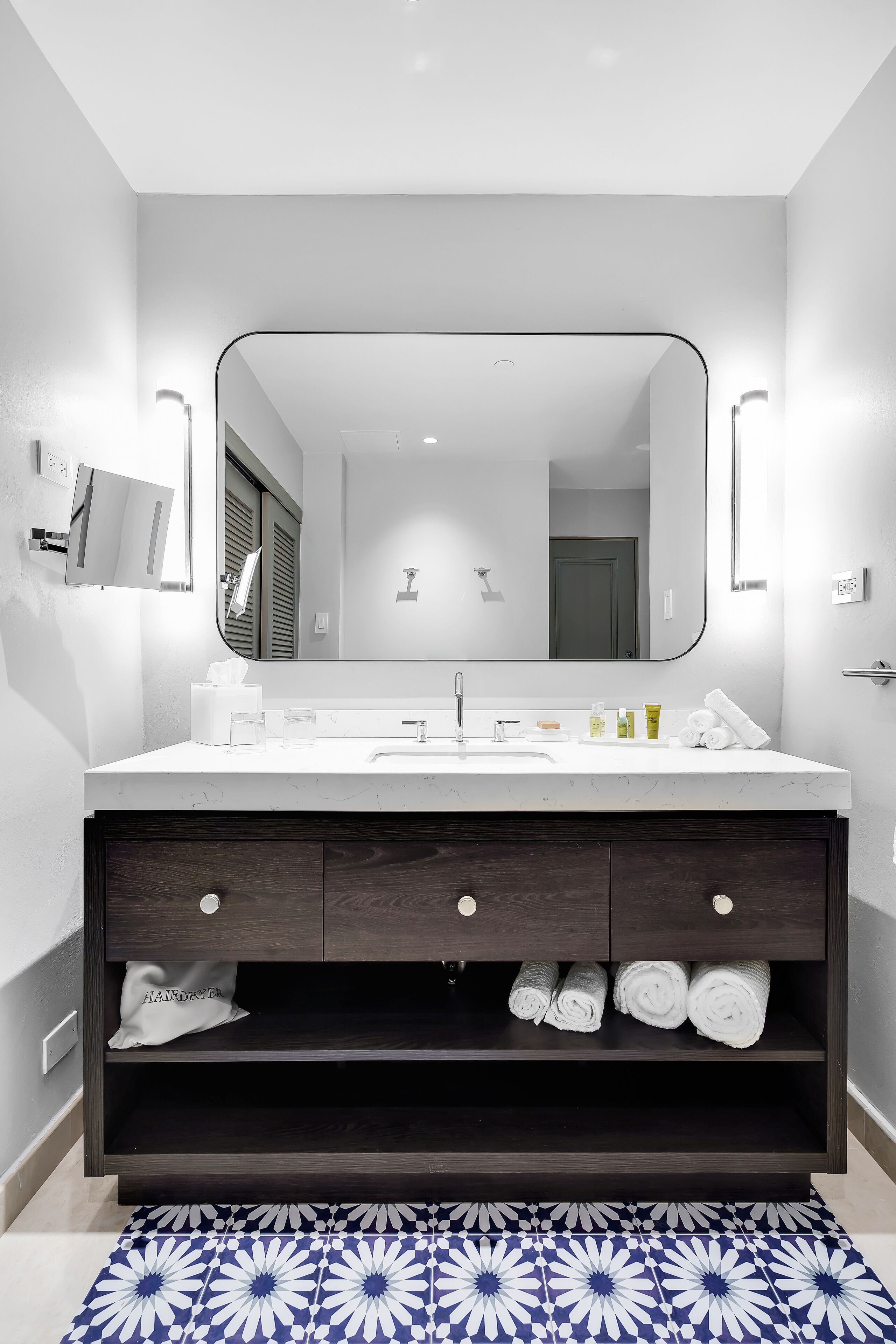 Un baño moderno con tocador blanco, mueble de madera oscura y un espejo grande.
