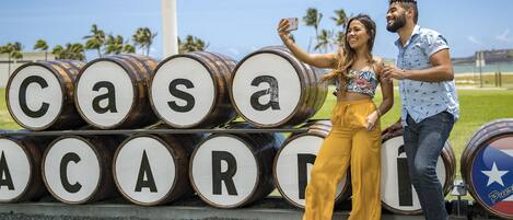 A couple taking a selfie in front of barrels with letters spelling out "Casa Acadia."