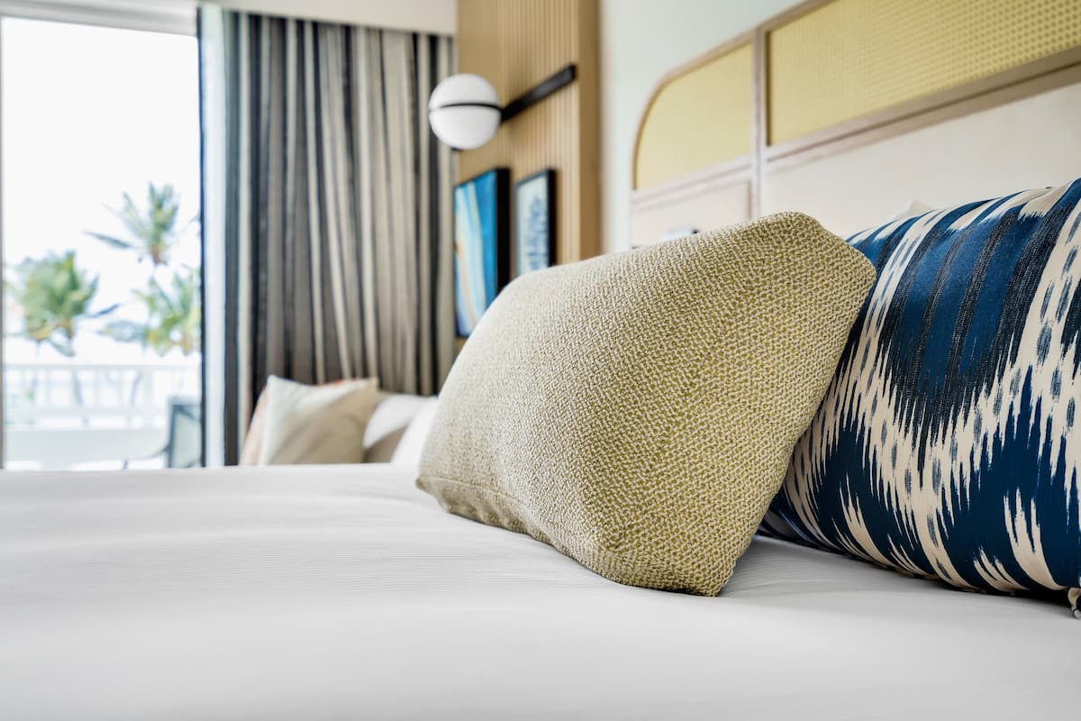 Habitación de hotel con cama, almohadas, una ventana con cortinas y una lámpara en la pared.