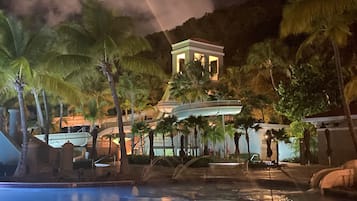 A resort with a swimming pool, palm trees, and a building with a balcony.