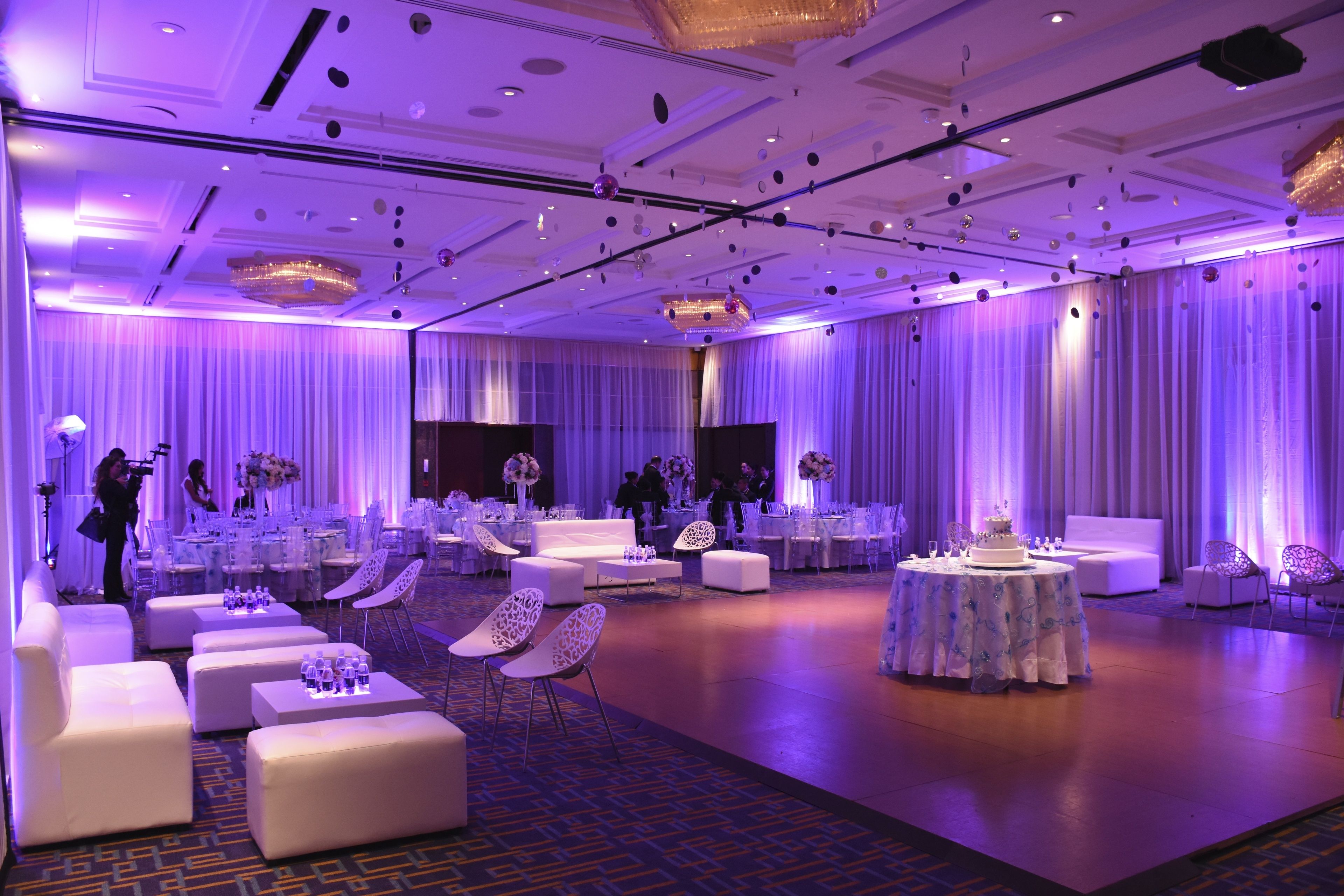 Une salle de bal spacieuse, meublée de mobilier blanc, avec des tables rondes et un arrangement floral central.