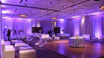 Une salle de bal spacieuse, meublée de mobilier blanc, avec des tables rondes et un arrangement floral central.