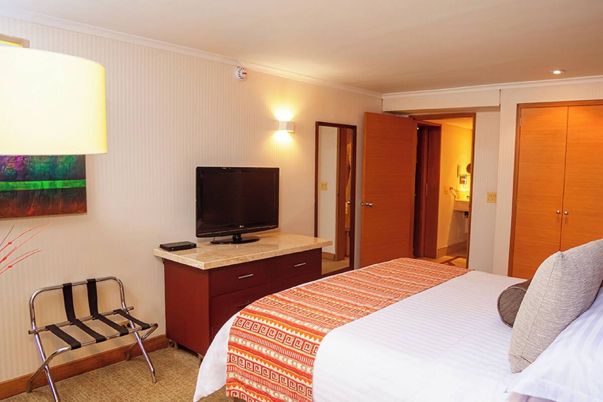 Habitación de hotel con cama, televisor en una cómoda, escritorio, silla y armario.