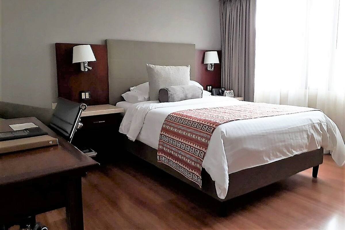 Habitación de hotel con cama, dos mesitas de noche, un escritorio y una silla.