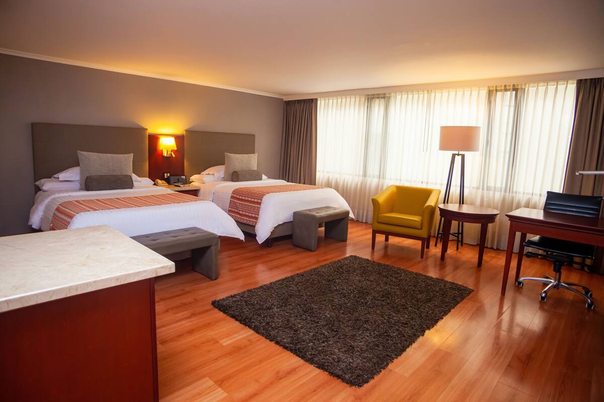 Habitación de hotel con dos camas, un escritorio, una silla y una lámpara.