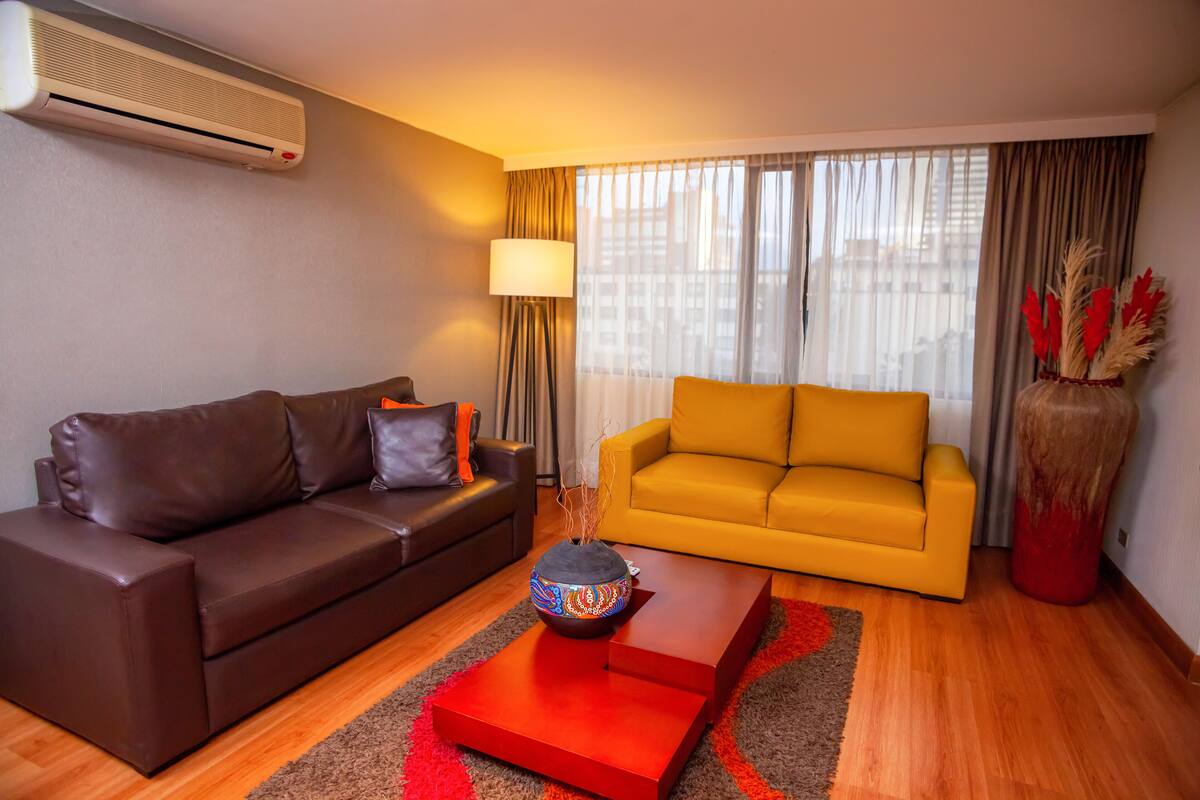 Una sala de estar moderna con un sofá de cuero marrón, un sofá amarillo y una mesa de centro roja con un cuenco decorativo.
