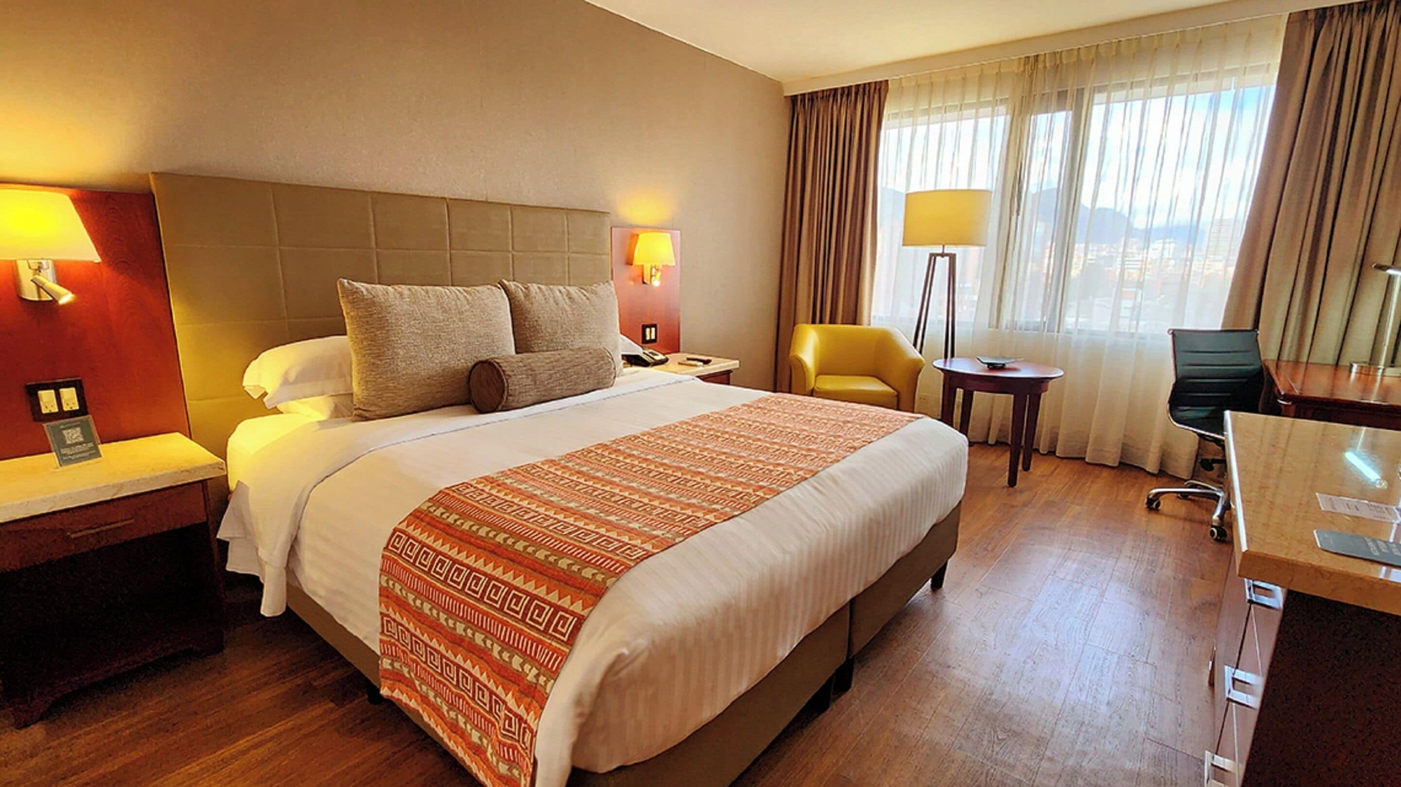 Una habitación de hotel con una cama grande, dos mesitas de noche, un escritorio, una silla y una lámpara.