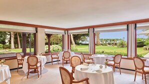 Un espace repas avec des tables et des chaises rondes, de grandes fenêtres avec des rideaux et une vue sur un jardin aménagé.
