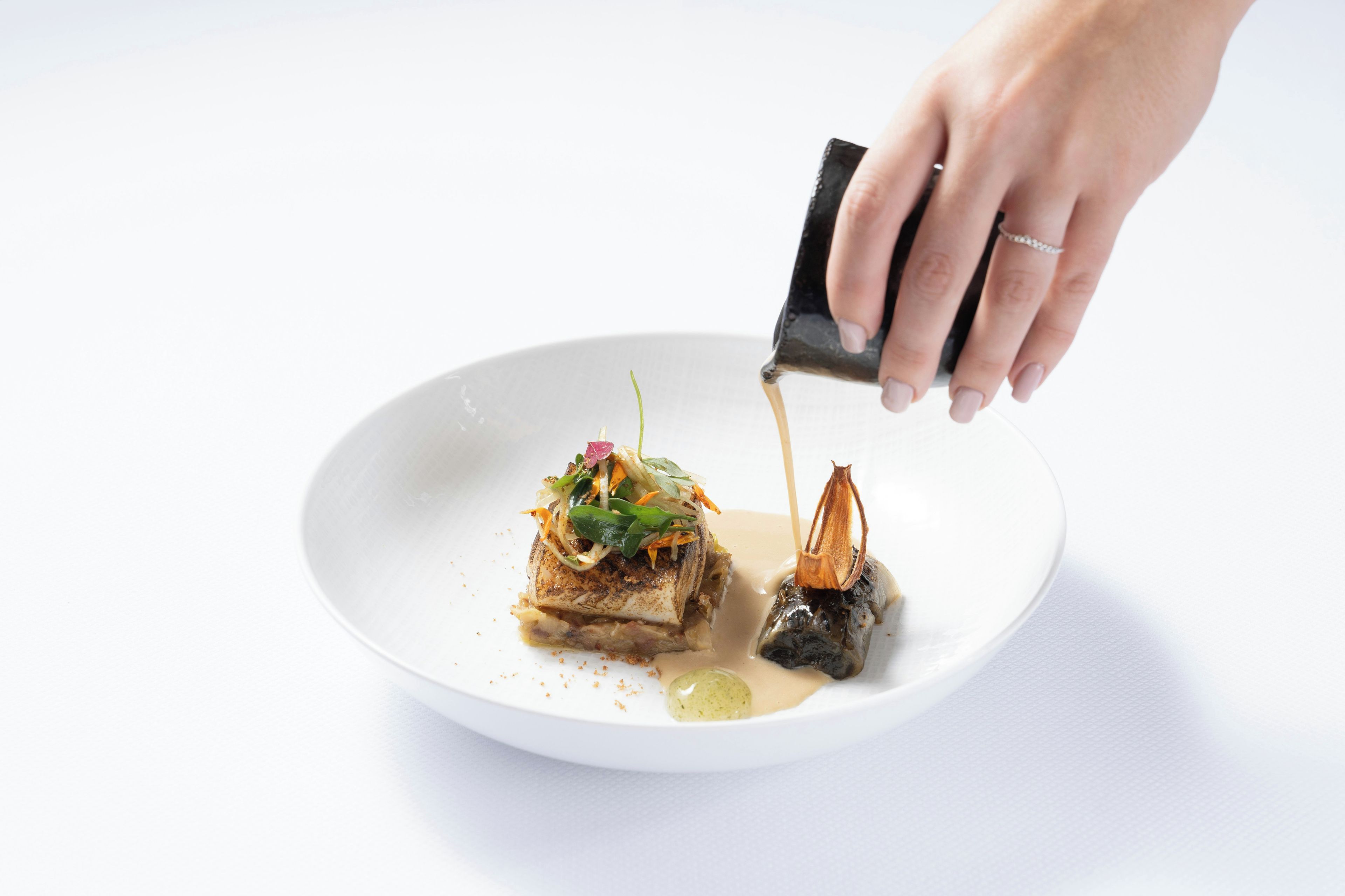 A hand pouring sauce onto a plate with food.