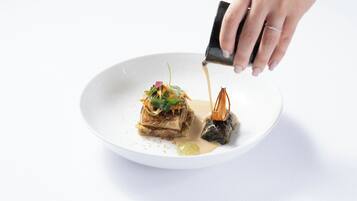 A hand pouring sauce onto a plate with food.