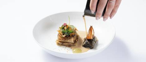 A hand pouring sauce onto a plate with food.
