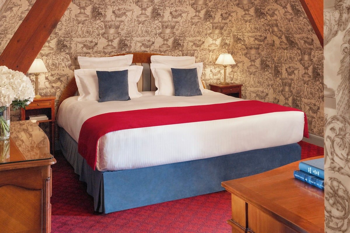 A bedroom with a large bed, a red carpet, and patterned wallpaper.