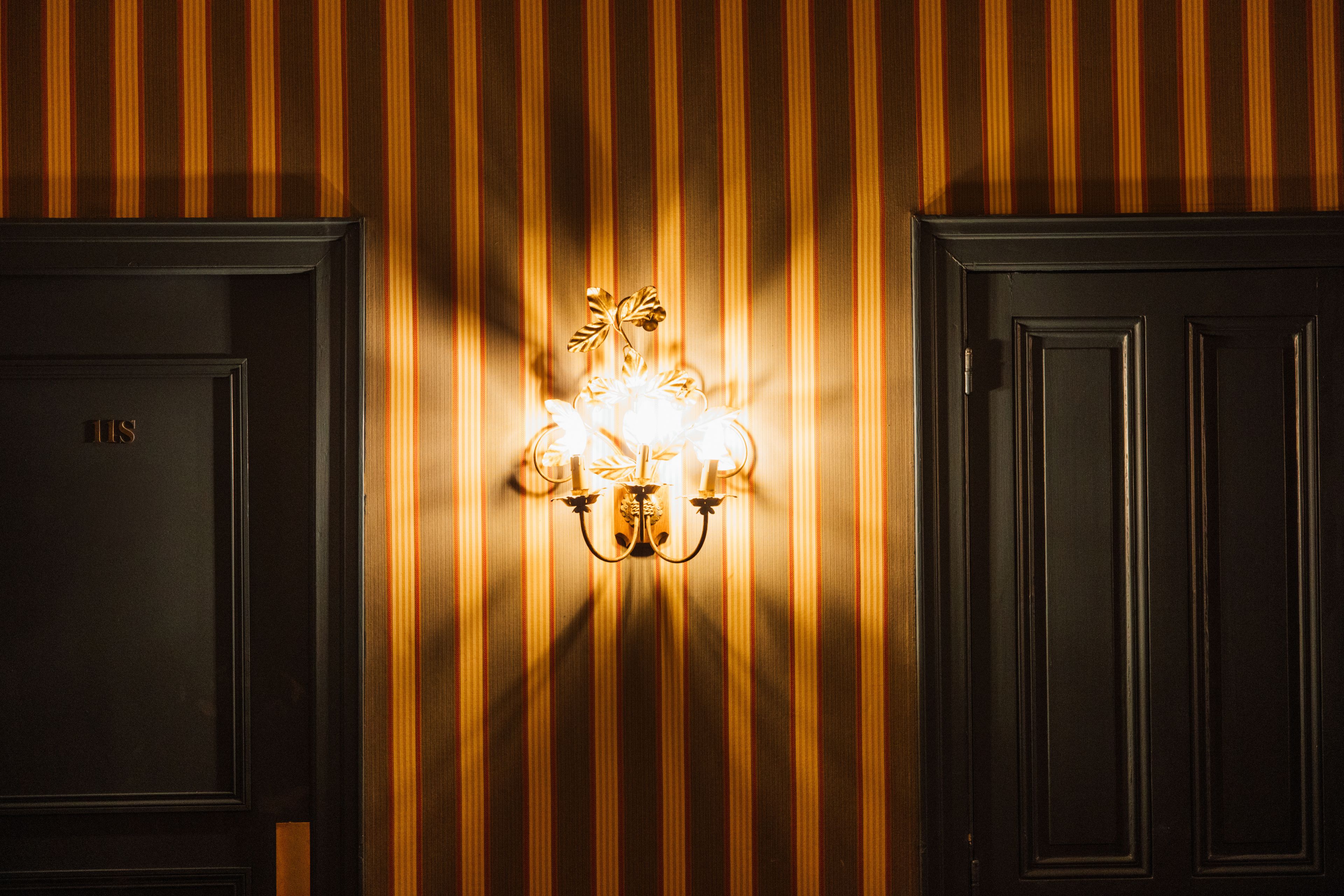 A wall-mounted light fixture with a decorative design, positioned between two dark wooden doors.