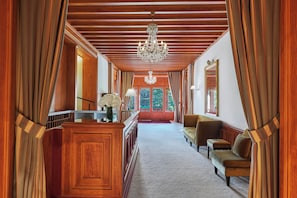 Een hal met houten lambrisering, een kroonluchter, een bank en een spiegel.