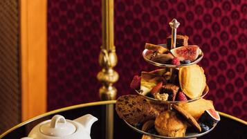 A tea set with a teapot and cups on a table, accompanied by a tiered tray of pastries and a small bowl of jam.