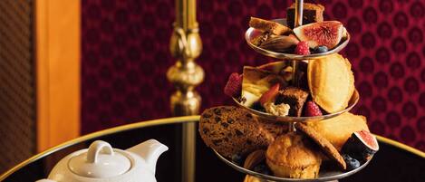 A tea set with a teapot and cups on a table, accompanied by a tiered tray of pastries and a small bowl of jam.