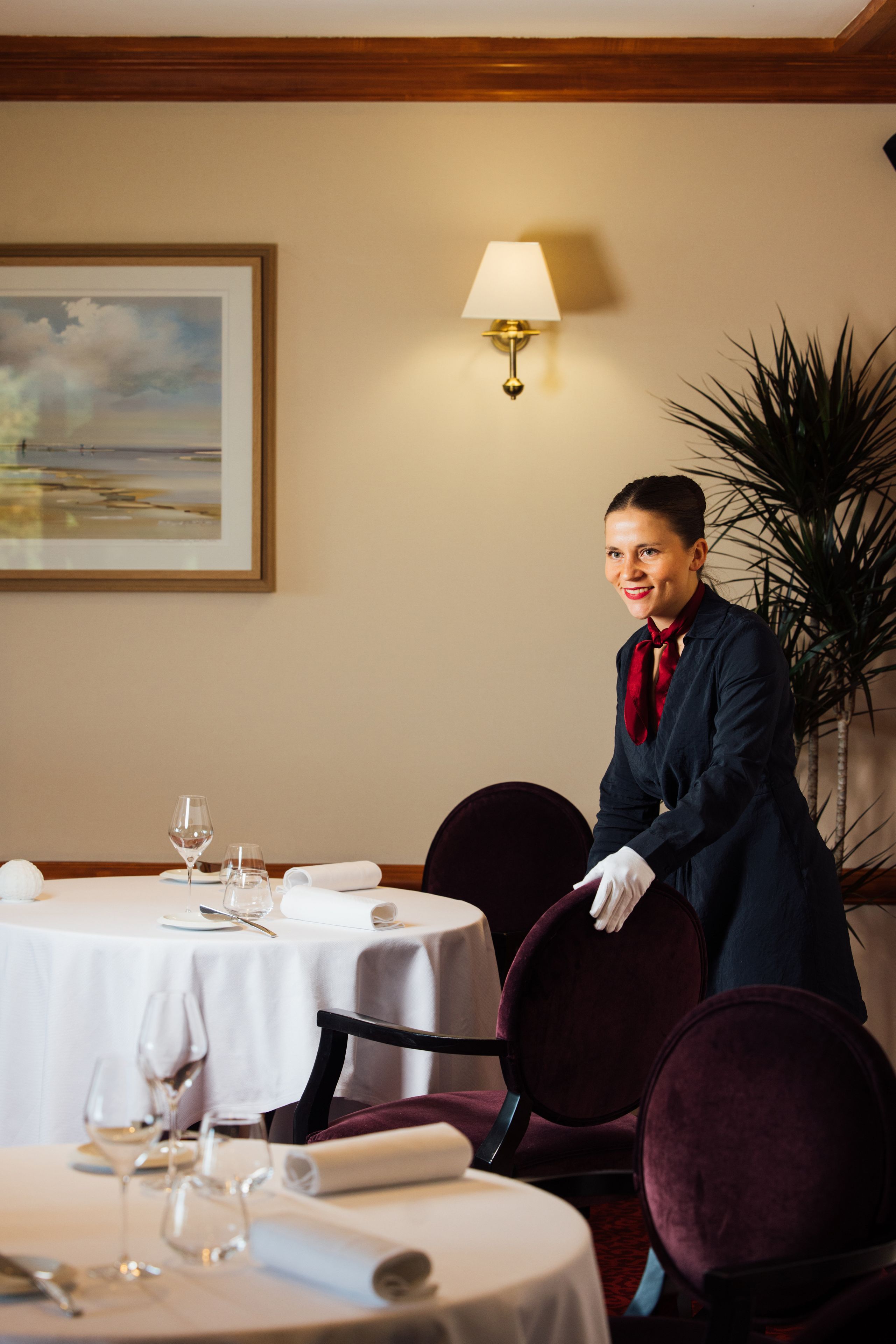 Une chambre d’hôtel avec une table à manger dressée pour un repas, un tableau accroché au mur et une lampe.
