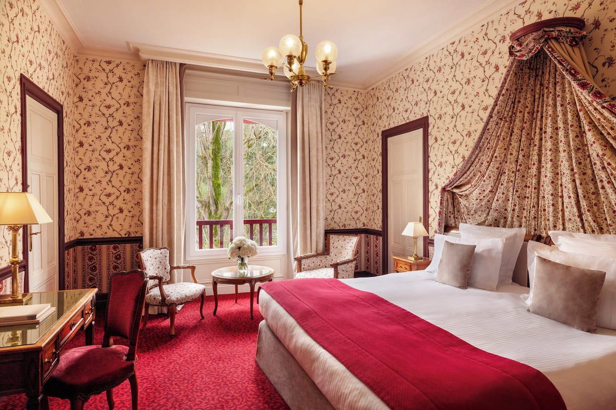 A hotel room with a large bed, two chairs, a desk, and a window with curtains.