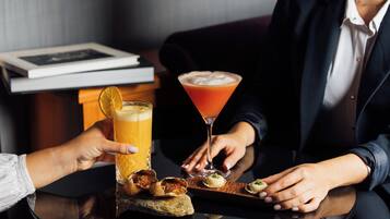 A person holding a glass of orange juice and a martini glass with a cocktail on a table.