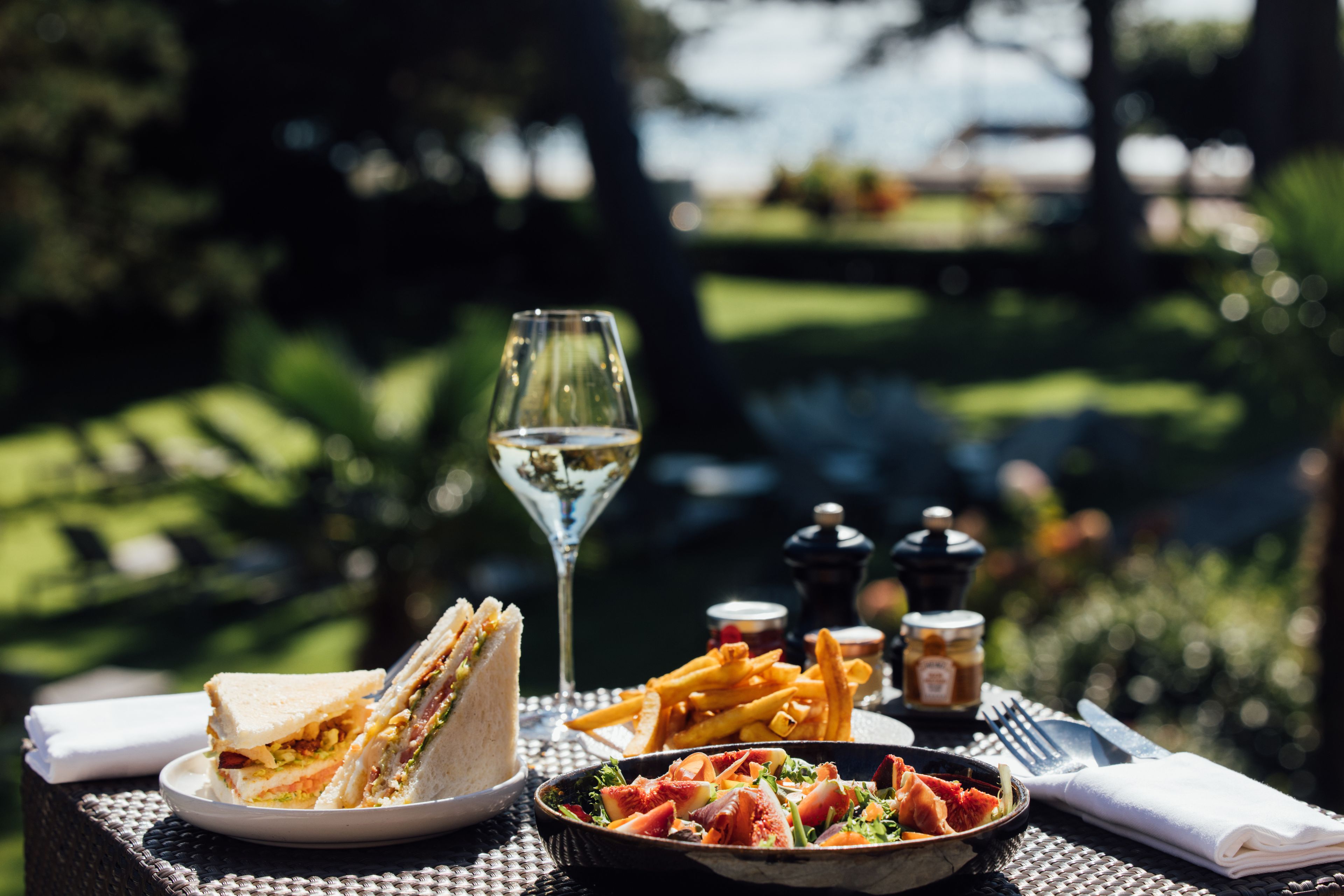 A table set with a sandwich, fries, a salad, a wine glass, and condiments.