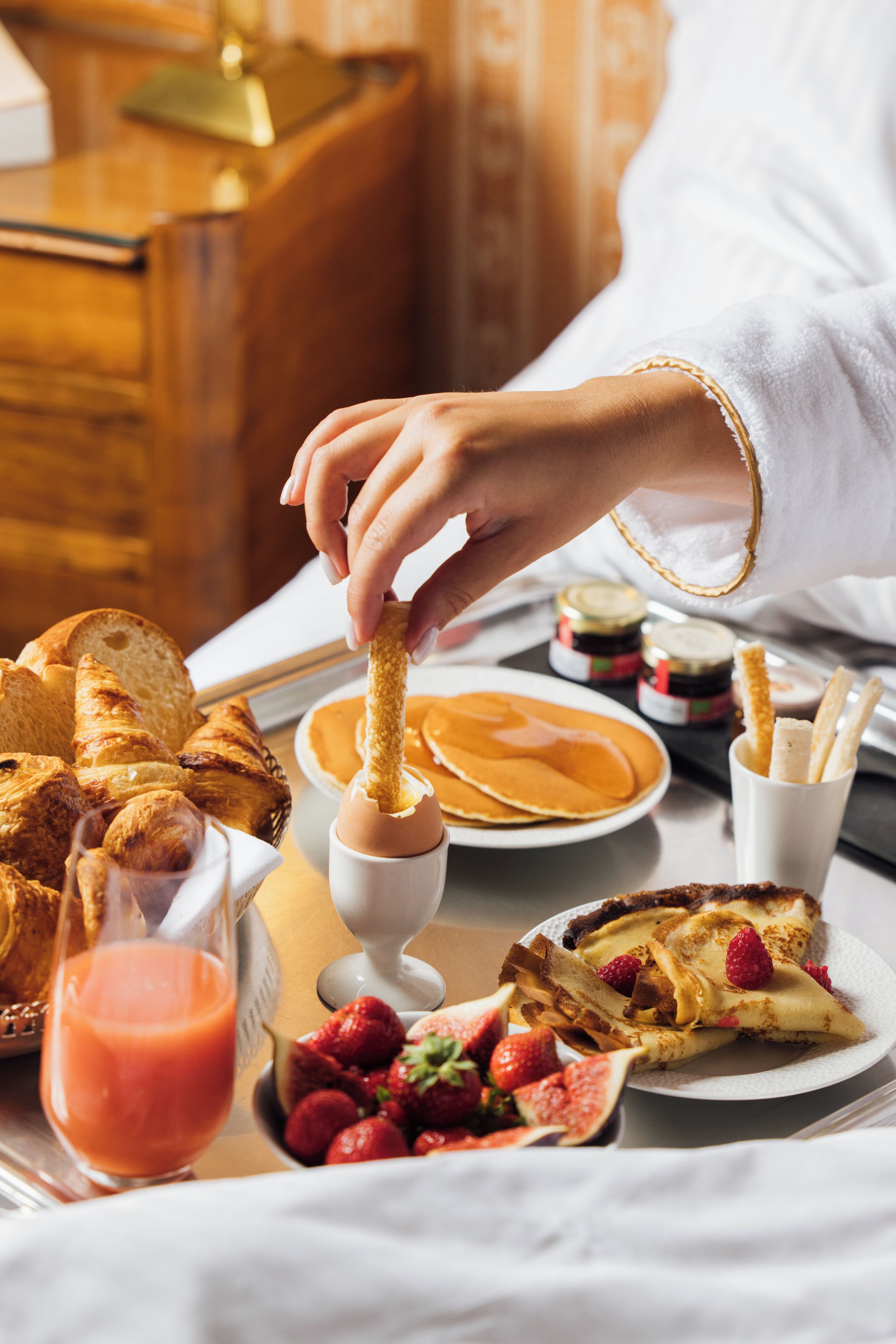 Un plateau de petit-déjeuner avec des croissants, des crêpes, des fraises et un verre de jus d’orange.