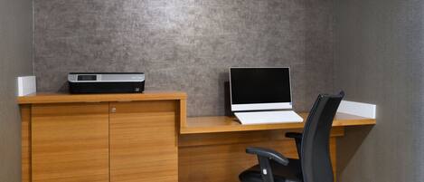 A workspace with a wooden desk, a laptop, a printer, and a black office chair.