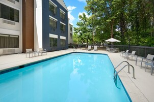 Una piscina rectangular con una escalera metálica, rodeada por un patio de concreto. Hay sillas de descanso y una mesita con sombrilla.