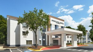 Et moderne hotel med overdækket indgang, markeret handicapparkering og en klar himmel.