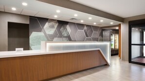 Et hotellets reception område med en træreception, væg med geometrisk mønster, og moderne indretning.