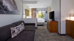 A hotel room with a sofa, a TV on a wooden stand, a bed with a window view, and a large painting on the wall. - SpringHill Suites by Marriott Pasadena Arcadia (Arcadia)