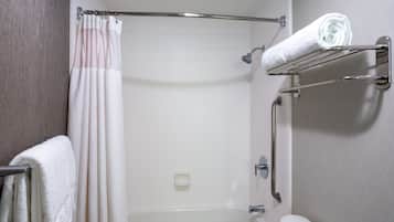 A shower area with a glass door, a towel rack with a folded towel, and a toilet with a paper towel holder.
