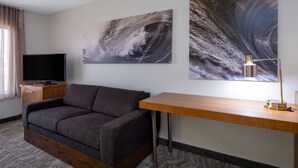 A modern hotel room with a grey sofa, a wooden desk, a flat-screen TV, and two abstract paintings on the wall. - SpringHill Suites by Marriott Pasadena Arcadia (Arcadia)