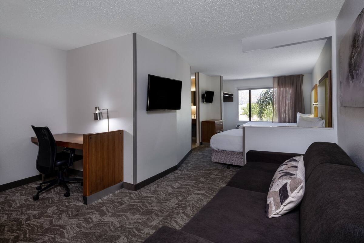 A hotel room with a desk, a bed, a sofa, a TV, and a window with curtains.