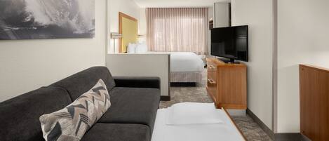 Una habitación de hotel con sofá, cama, televisión y un cuadro grande en la pared.