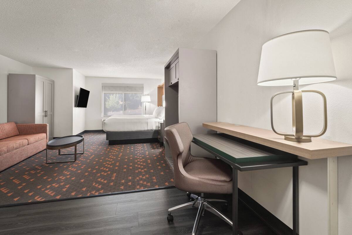 A hotel room with a bed, a desk with a lamp, a sofa, and a TV on the wall.